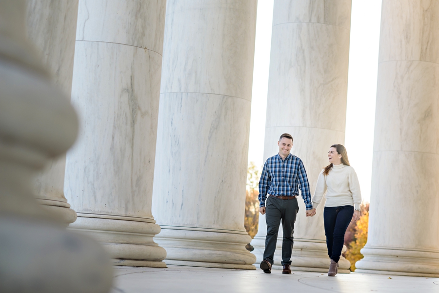 A cute couple walk along the columns holding hands.